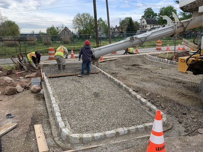 Concrete pumper truck delivers mix into a granite cobblestone curbed pad with workers