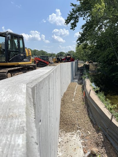 Long board-form concrete retaining wall with skid steer and equipment behind under sun