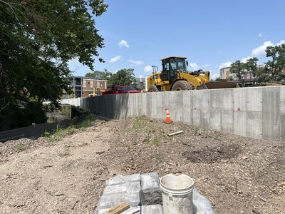 Wheel loader stages stone behind completed concrete retaining wall along urban edge