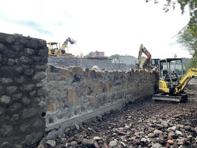 Newly veneered fieldstone retaining wall along rocky channel with excavators working behind