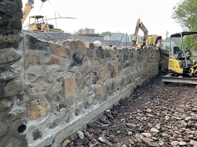 Long fieldstone retaining wall with fresh mortar joints and excavators staged above