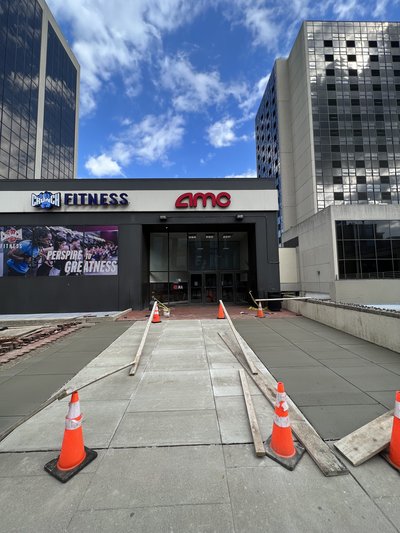 Freshly placed concrete sidewalk panels curing between cones outside commercial entrance under blue sky