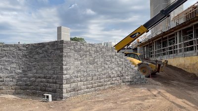 Tall stacked block retaining wall with telehandler and adjacent commercial building under construction