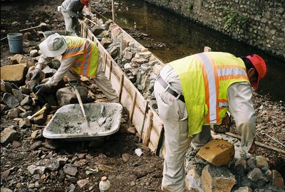 Workers in safety vests setting wood forms for stone wall along stream bank