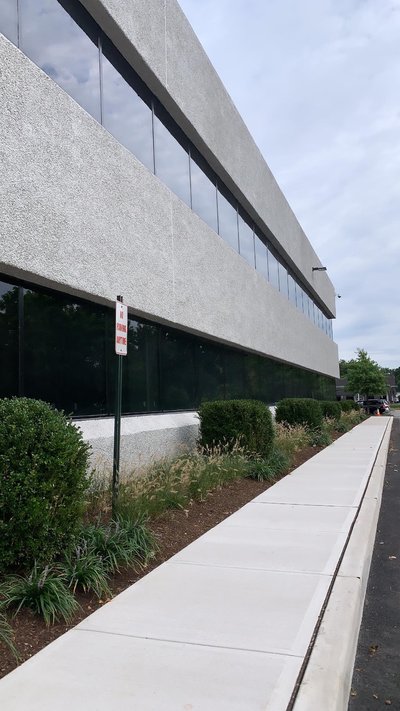 Newly poured concrete sidewalk along commercial building under overcast sky with landscaped plantings