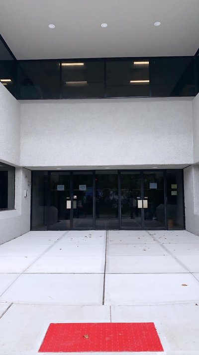 Concrete entrance plaza with red detectable warning pad outside double glass entry doors