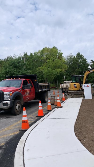 Curved concrete sidewalk pour with red dump truck and tracked excavator on site