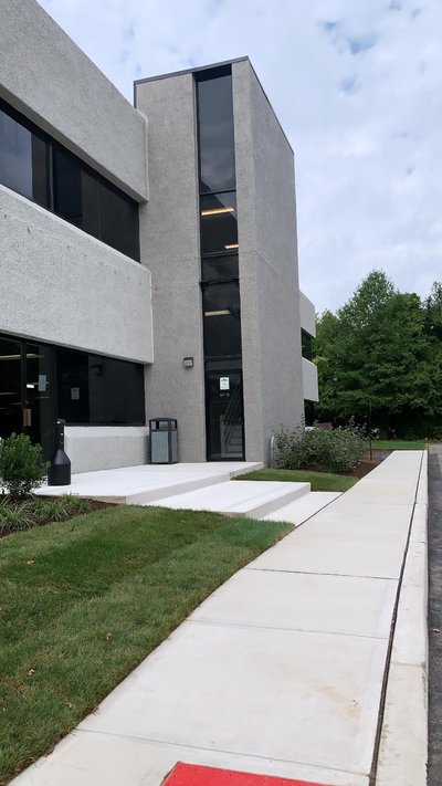 Concrete entrance steps and walkway beside modern stucco building with green lawn