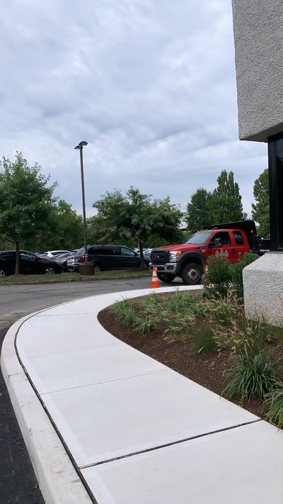 Curving concrete sidewalk along parking lot with red company dump truck parked nearby