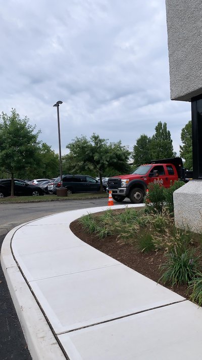 Curved concrete walkway beside parking lot with red dump truck and orange cone