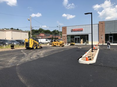Skid-steer loader and asphalt roller positioned on new pavement at a commercial retail plaza
