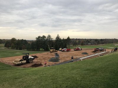 Roller compactor and trucks grading earthwork for cart path under cloudy fall sky