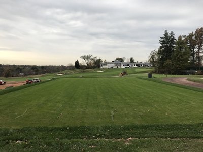 Wide turf fairway with backhoe at bunker edge and clubhouse on horizon