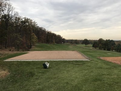 Sand-prepared tee box pad framed by curbs overlooking autumn fairway and woodland