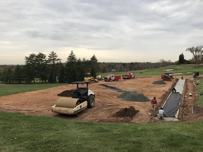 Roller and trucks staging cart path subgrade with gravel piles on fall fairway