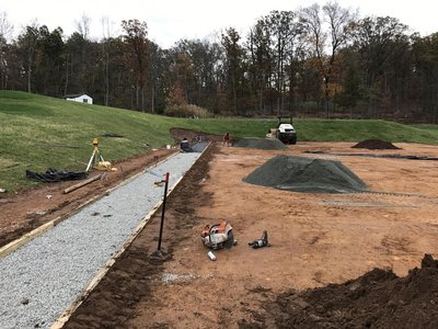 Gravel-filled formed cart path section with concrete saw and aggregate piles on hillside