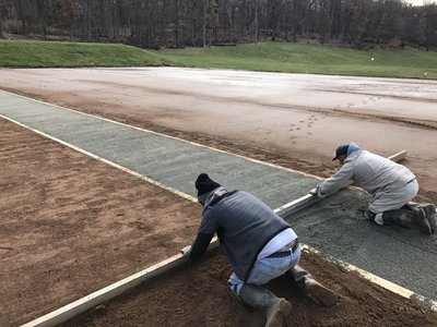 Two workers screeding base material between curb forms beside freshly poured concrete pad