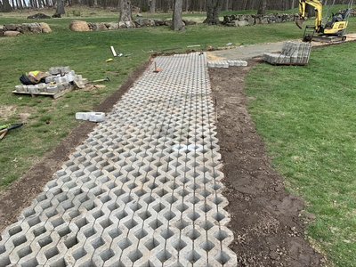 Honeycomb permeable concrete grid pavers laid across grass with mini excavator in background