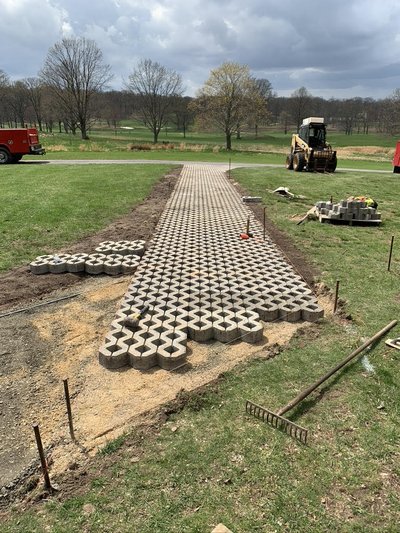 Permeable grid paver cart path under installation on golf course with skid steer nearby