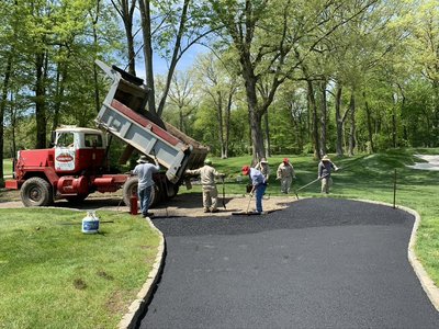 Crew finishing asphalt cart path beside red dump truck on tree-lined fairway